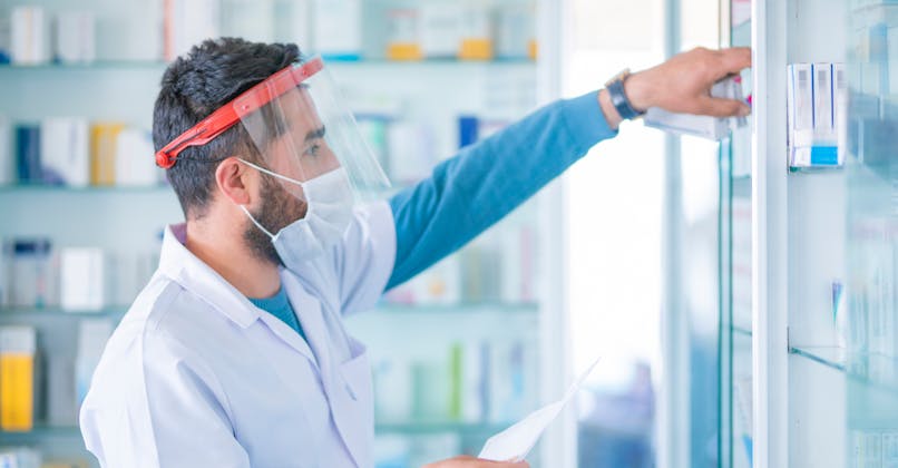 Un pharmacien avec une visière et un masque.