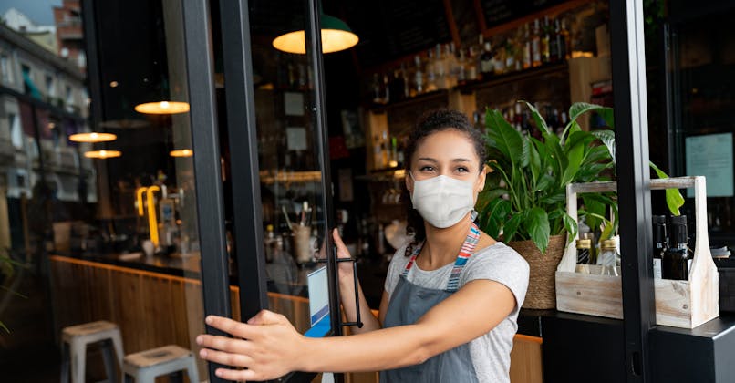 Une femme avec un masque de protection ouvre la porte d'un restaurant