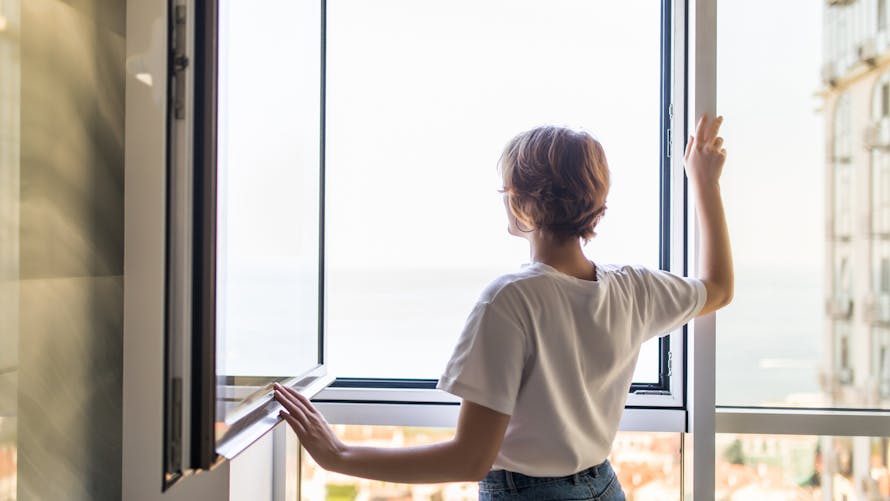 Une femme ouvre sa fenêtre pour aérer son appartement