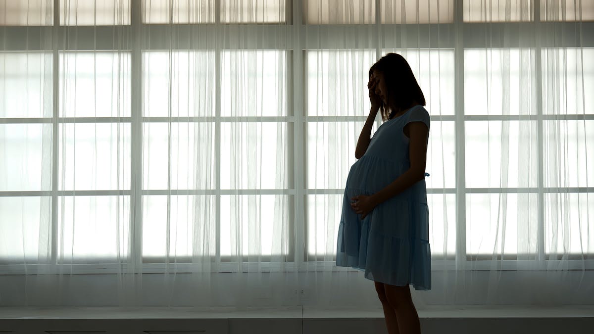 Femme enceinte dépressive qui se tient devant une fenêtre