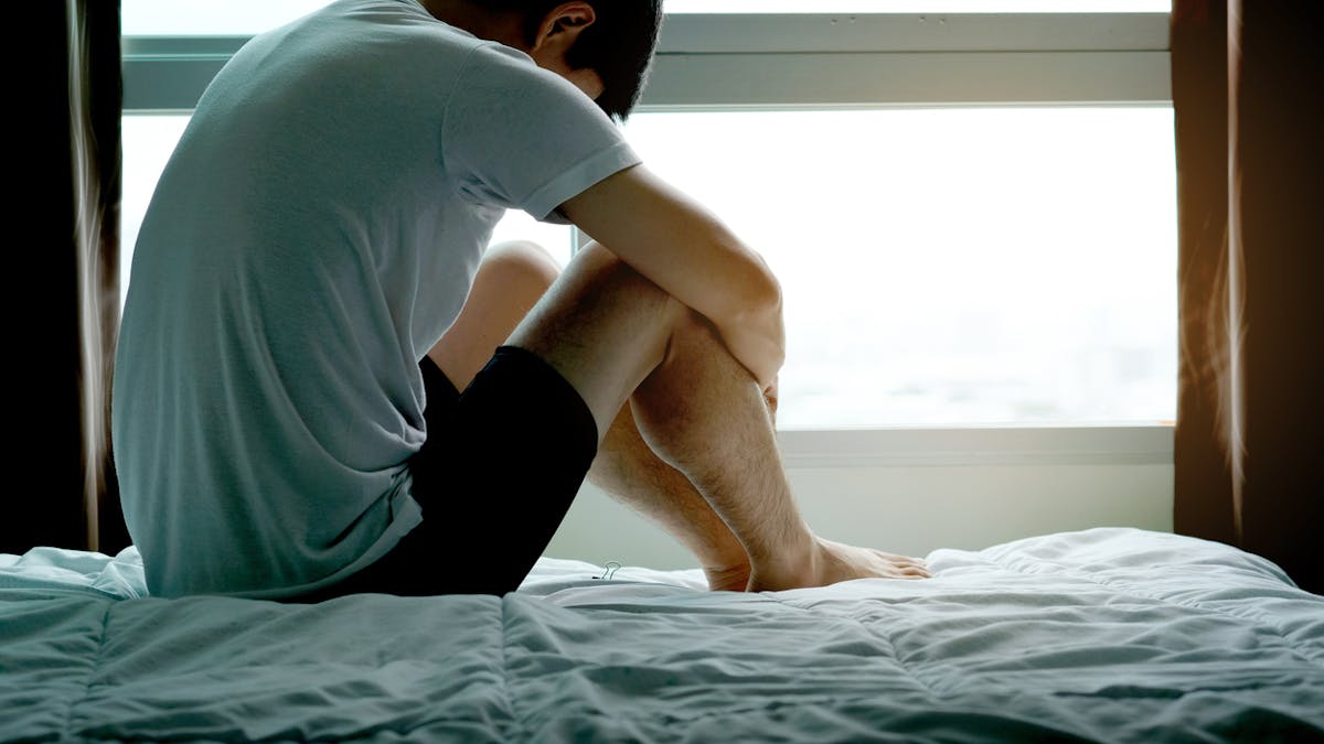 homme assis sur une lit et stressé à cause d'un trouble sexuel