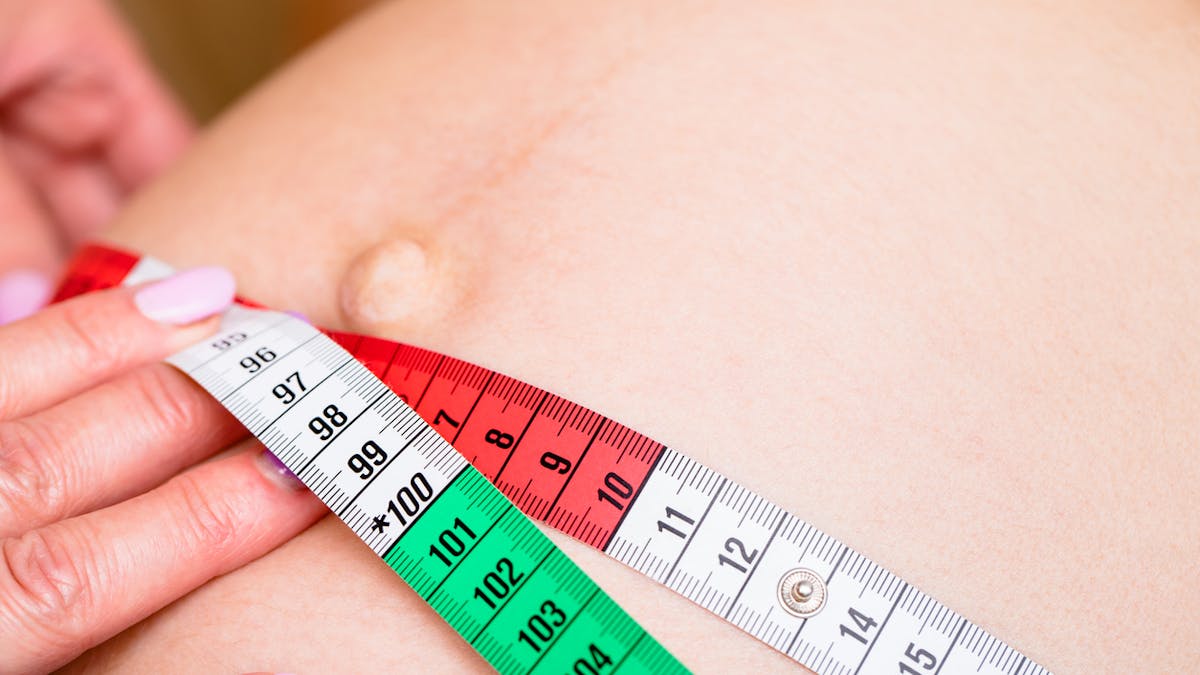 Gynécologue mesurant le ventre de la femme enceinte avec un mètre ruban pendant la visite prénatale