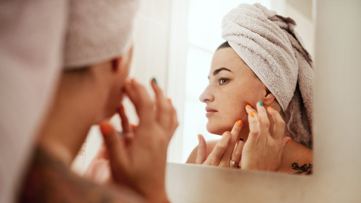 Femme atteinte d'acné qui se regarde dans un miroir.