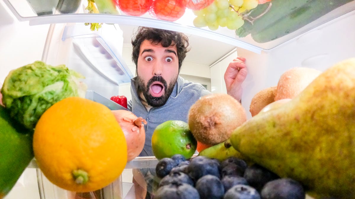 Un jeune homme ouvre son frigo et a peur des fruits qui s'y trouvent (carpophobie)