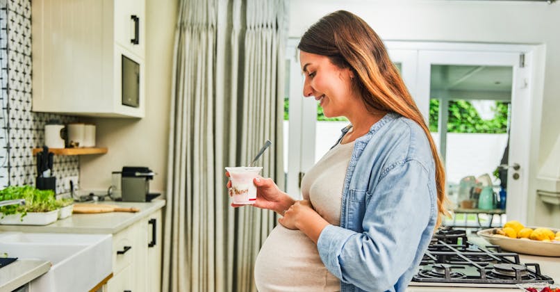 Une femme enceinte mange un yaourt dans sa cuisine