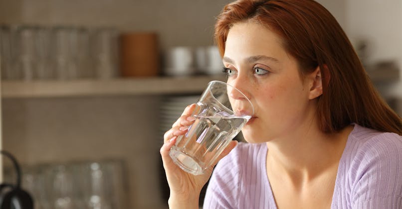 Une jeune femme boit un verre d'eau dans sa cuisine