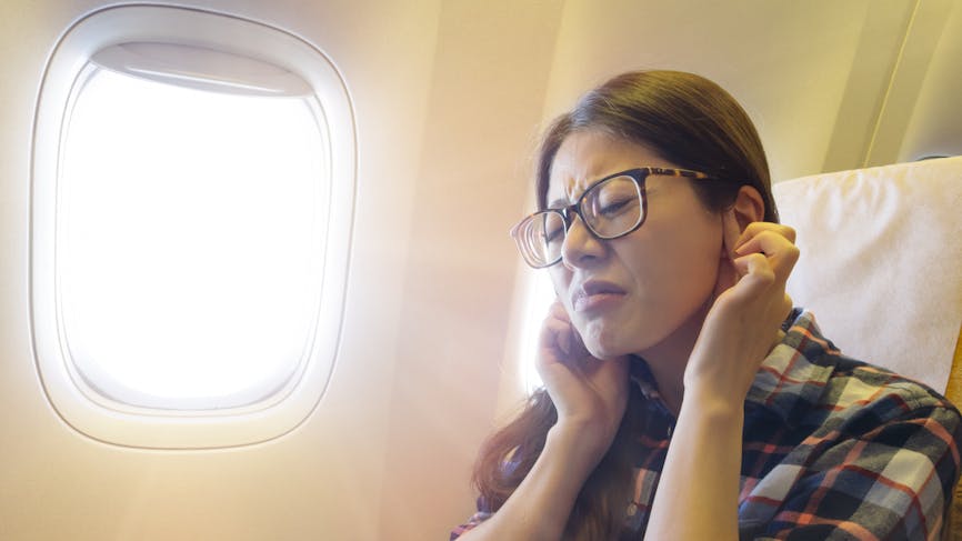 femme ayant mal aux oreilles en avion