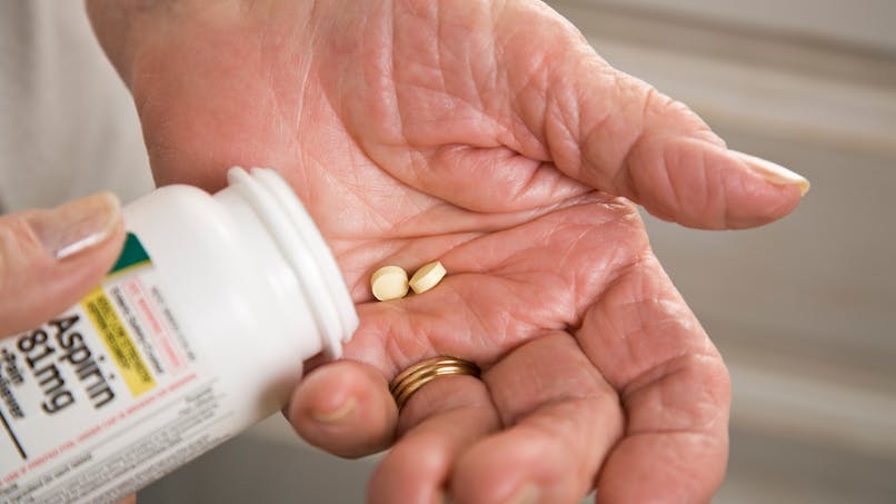 main d'une personne âgée qui prend deux cachets d'aspirine 