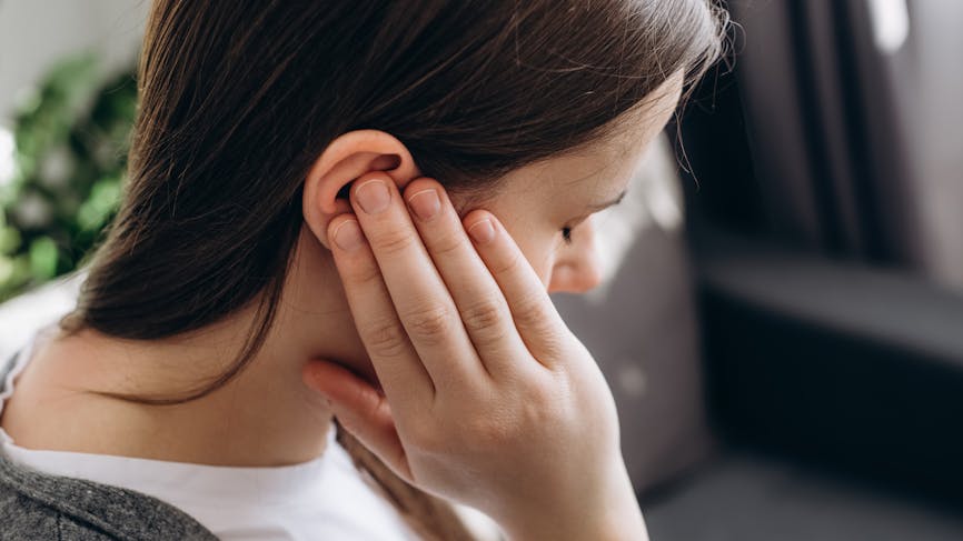 Gros plan d’une jeune femme brune tenant une oreille douloureuse, ressentant soudainement une forte douleur.