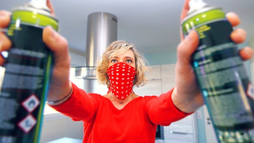 Femme avec un foulard sur le bas du visage pour se protéger des émanations d'insecticide. Elle tient deux bouteilles d'insecticide aérosols. 