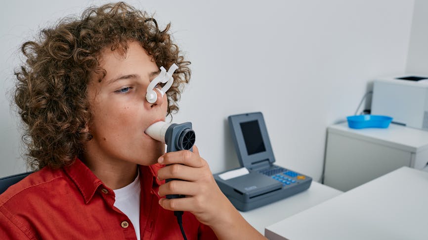 Petit garçon aux cheveux bouclés qui effectue un test de la fonction pulmonaire et une spirométrie à l’aide d’un spiromètre à la clinique médicale. 
