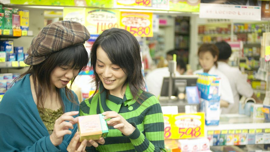 Deux jeunes nippones souriantes regardent une boîte de médicament en pharmacie