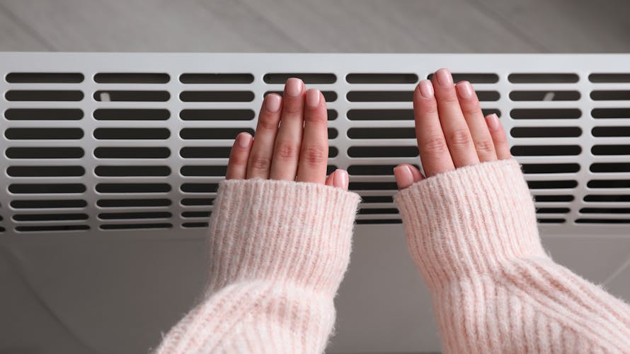 Une jeune femme se réchauffe les mains devant un radiateur