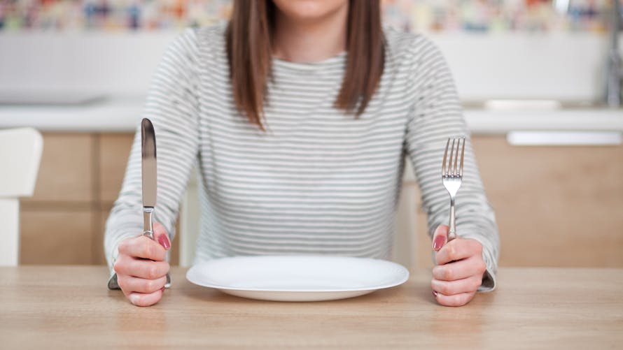 femme devant son assiette vide avec les couverts en l'air montrant qu'elle veut manger. 