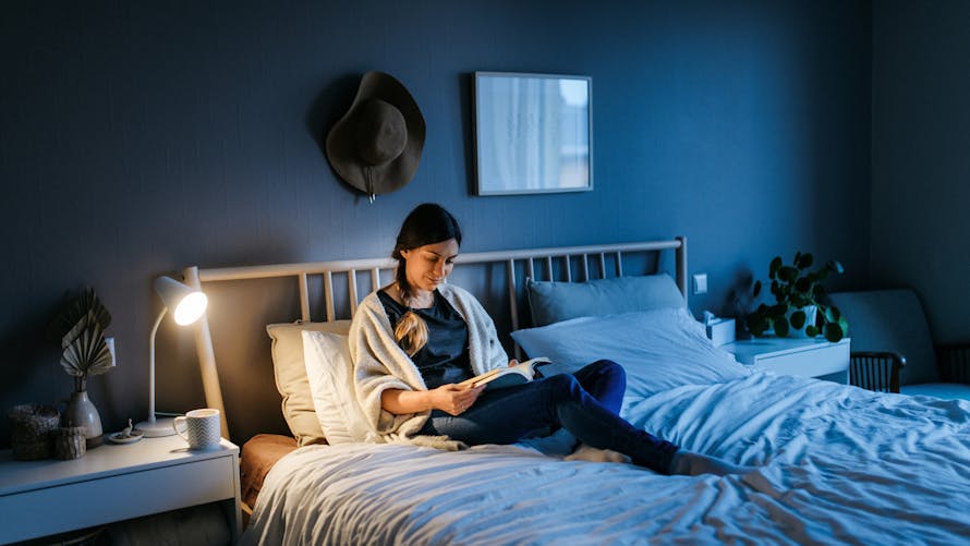 Une femme lit un livre dans son lit en début de soirée