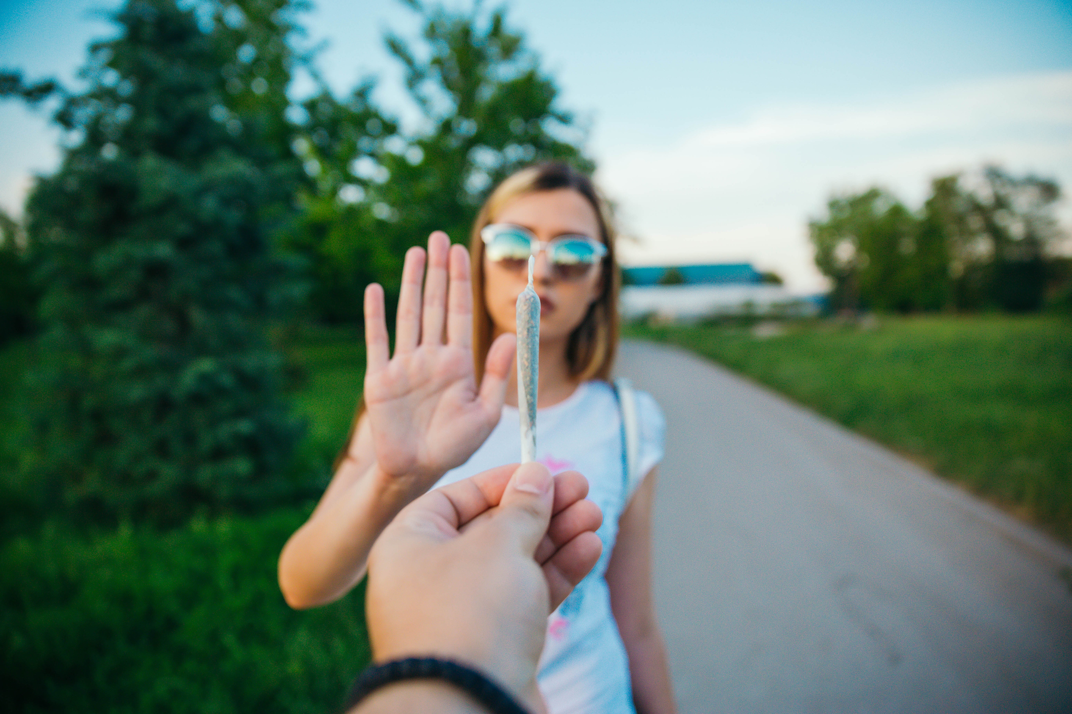 Femme refusant un joint, main levée en signe de refus, en extérieur.