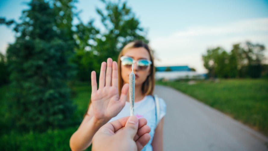 Femme refusant un joint, main levée en signe de refus, en extérieur.