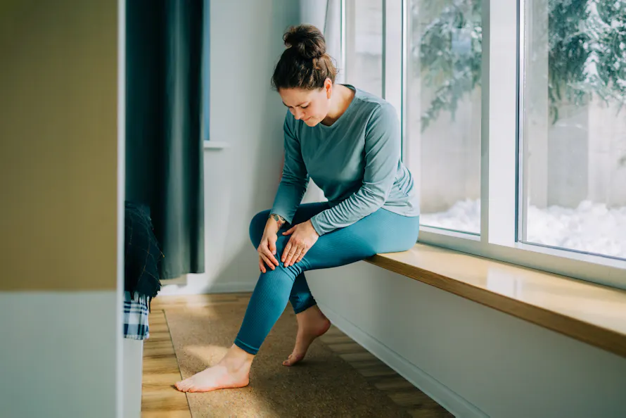 Une femme pensive assise sur un banc, regardant par la fenêtre d'une maison.