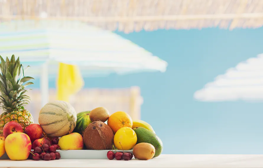 Assortiment de fruits tropicaux sur une table en bord de mer avec parasols en arrière-plan.