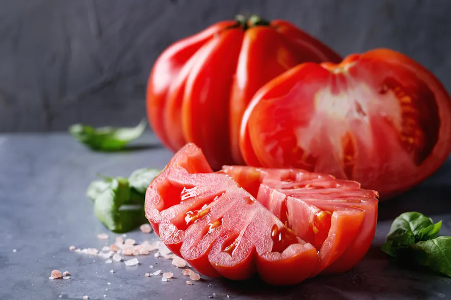 Tomates anciennes tranchées sur une table avec du sel et quelques feuilles de basilic.