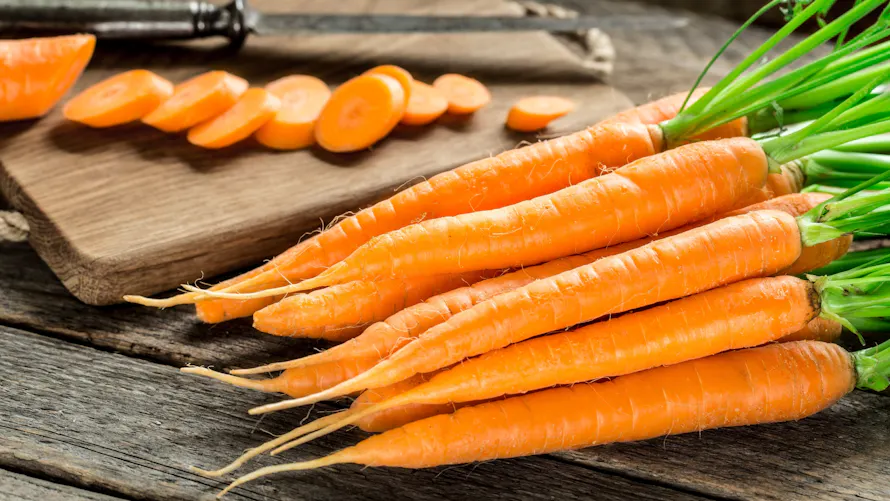 Des carottes fraîches sur une table en bois avec une planche de découpe.