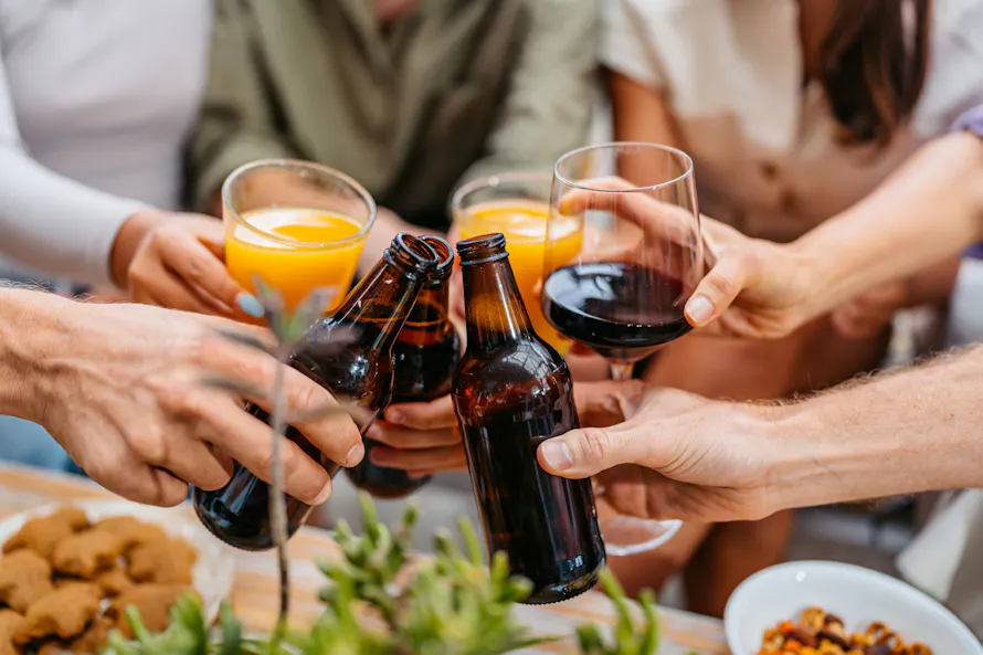 Des amis trinquent avec des verres de vin, de jus d'orange et des bières.